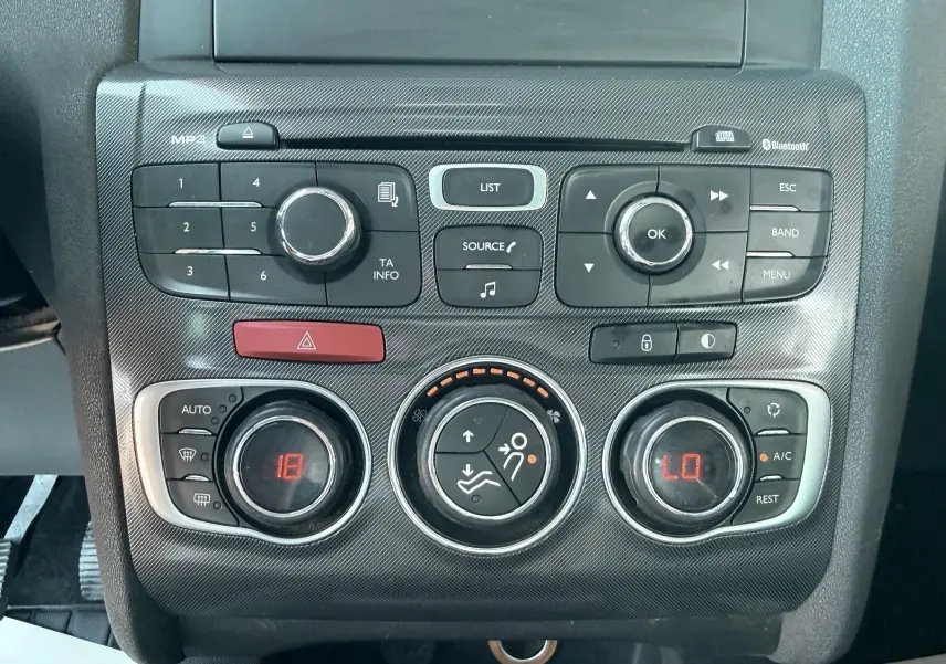 Vue rapprochée de la console centrale noire avec commandes de climatisation et radio d’une Citroën C4 gris 2011.