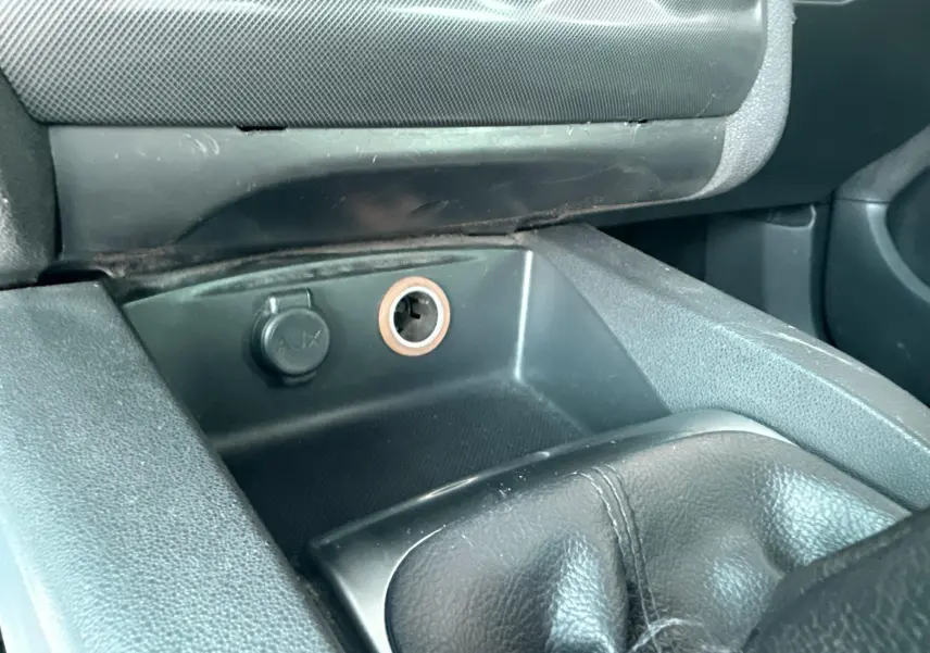 Gros plan sur la console centrale noire de la Citroën C4 2011, montrant la prise AUX et l’allume-cigare.