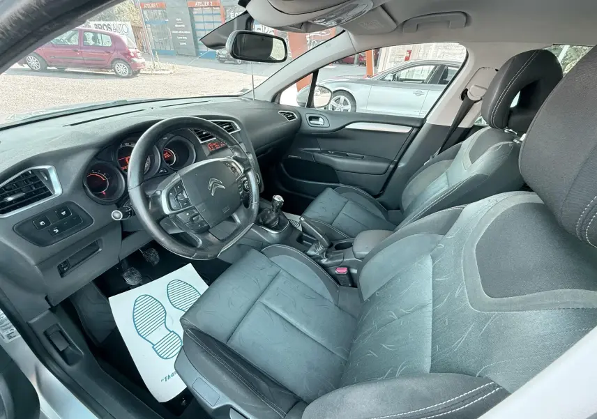 Vue intérieure côté conducteur de la Citroën C4 gris, montrant le volant, la boîte manuelle et les sièges tissu noirs.
