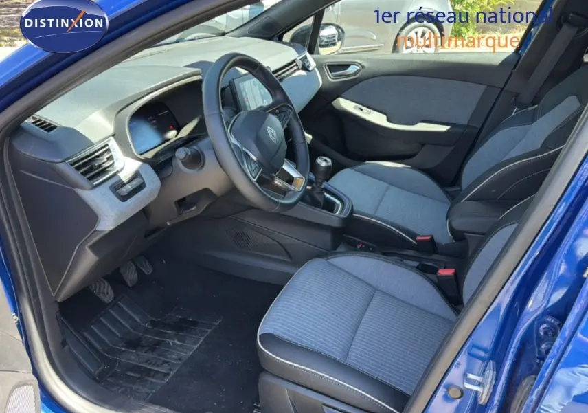 Vue intérieure côté conducteur d'une Renault Clio 2025 bleu Iron Metal, sièges tissu gris et volant cuir multifonction.