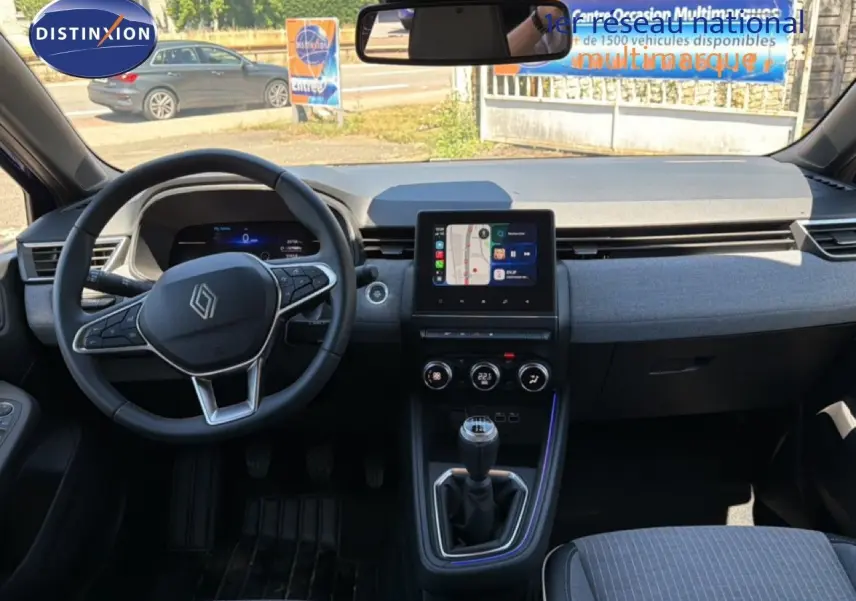 Vue intérieure avant de la Renault Clio 2025 avec tableau de bord moderne, écran tactile et volant multifonction.