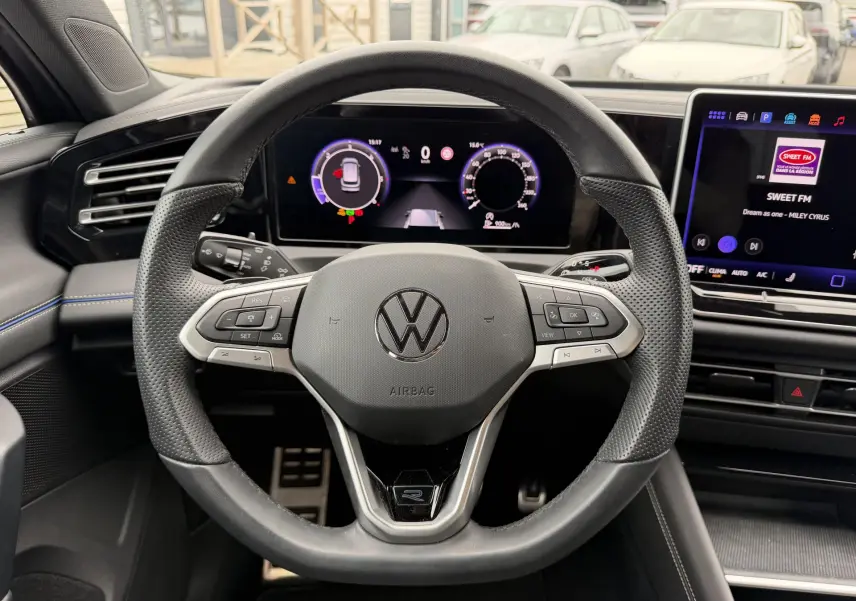 Vue intérieure centrée sur le volant multifonction cuir du Volkswagen Tiguan 2025 avec tableau de bord digital et écran tactile.