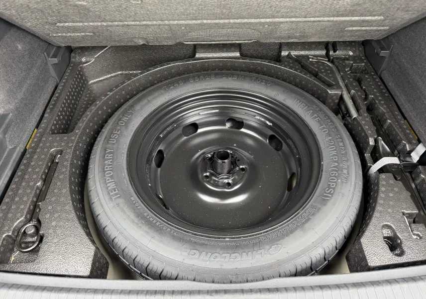 Gros plan sur la roue de secours compacte noire dans le coffre du Volkswagen Tiguan gris 2025.