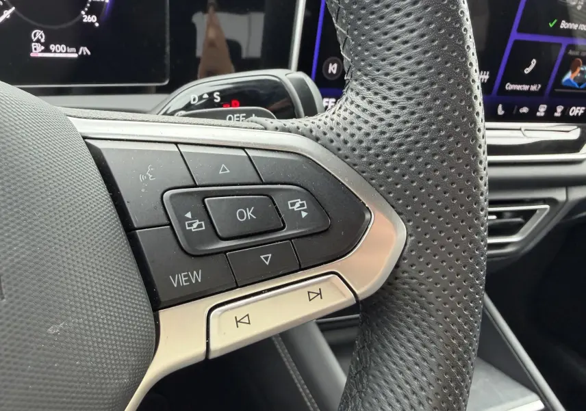 Gros plan sur la partie gauche du volant cuir perforé du Volkswagen Tiguan 2025 avec commandes multifonctions et tableau de bord numérique.