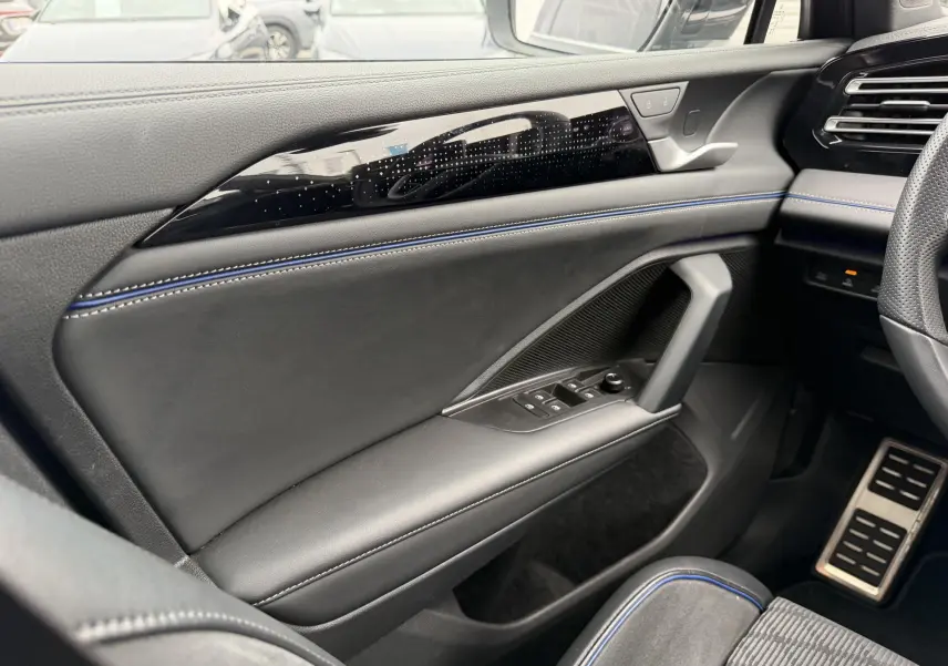 Vue intérieure côté gauche du Volkswagen Tiguan 2025, avec garniture cuir noire et surpiqûres bleues sur la porte.