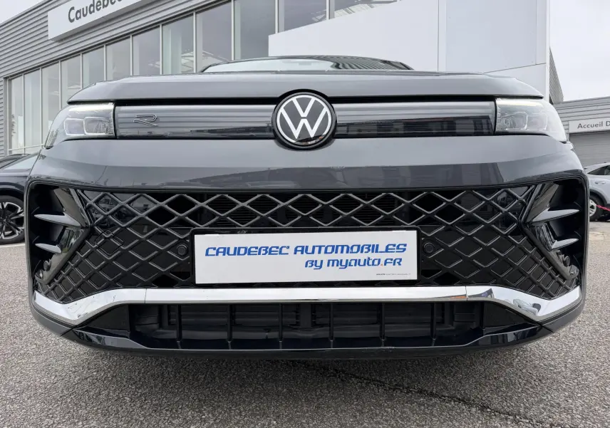 Vue frontale rapprochée du Volkswagen Tiguan gris 2025 avec calandre noire à motif losange et logo VW central lumineux.