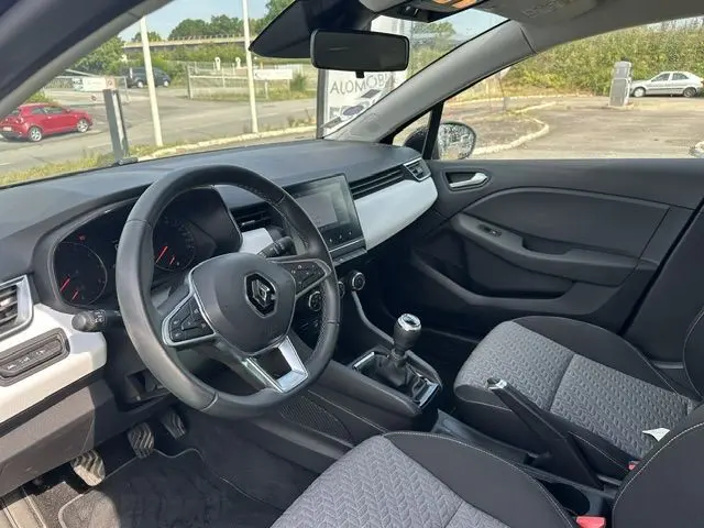 Vue intérieure côté conducteur de la Renault Clio noire 2022, volant multifonction et levier de vitesse manuel visibles.