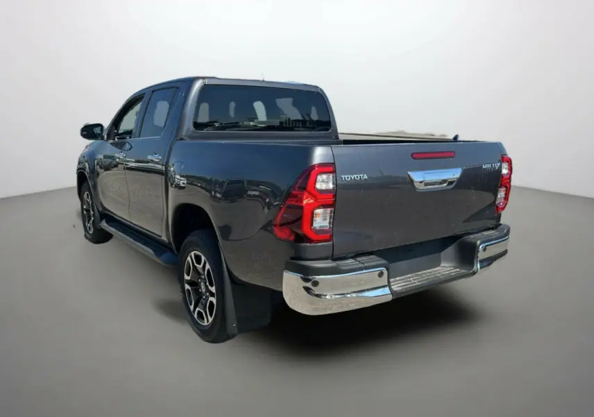 Toyota Hilux 4x4 gris atlas vu en 3/4 arrière droit, avec jantes alu 18 pouces et marchepieds visibles.