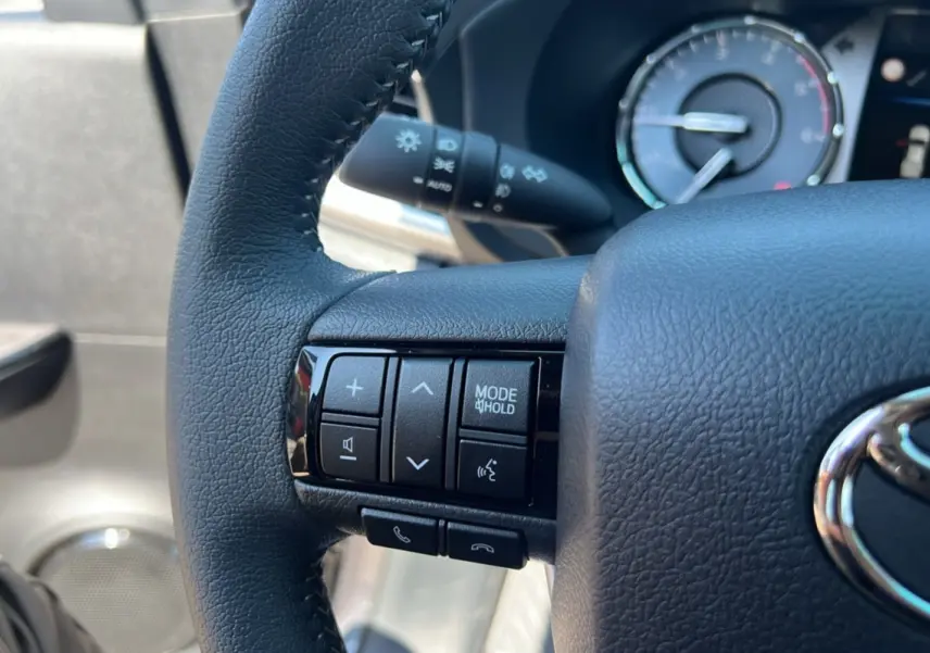 Gros plan sur le volant cuir noir du Toyota Hilux 2026, avec commandes multifonctions et tableau de bord en arrière-plan.