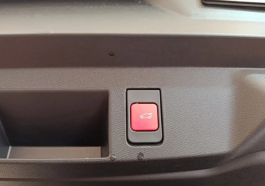 Bouton rouge d'ouverture électrique du coffre sur panneau intérieur noir d'une Citroën C5 Hybride 2026.