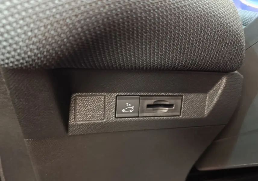 Gros plan sur le bouton d'ouverture du coffre noir situé sous le siège d'une Citroën C5 hybride verte.