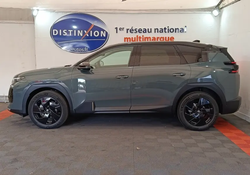 Vue de profil côté gauche d'un Citroën C5 hybride vert avec jantes noires et toit noir en intérieur showroom.