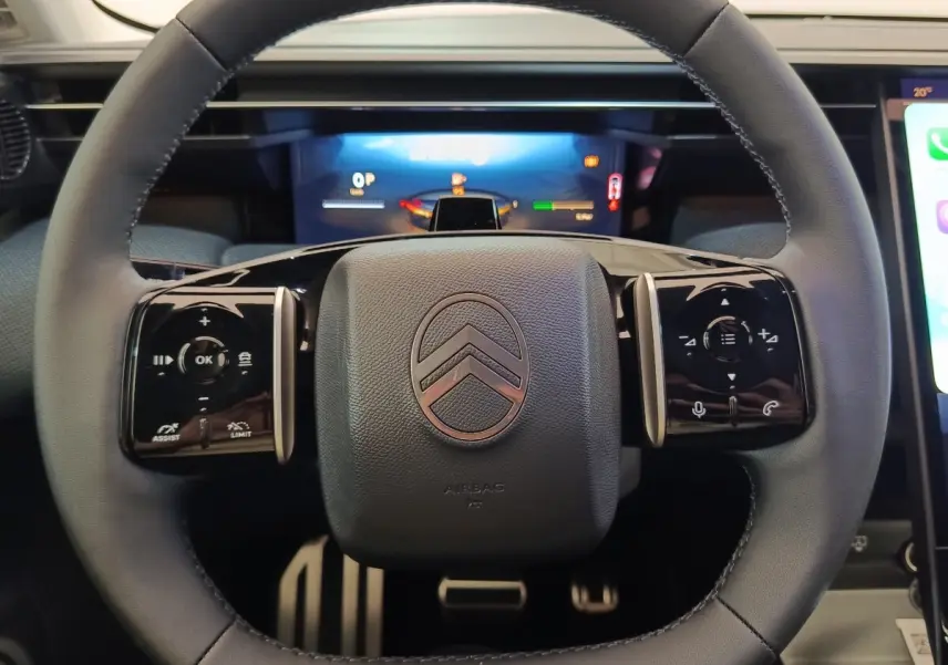 Vue rapprochée du volant noir de la Citroën C5 hybride 2026 avec commandes multifonctions et logo central.