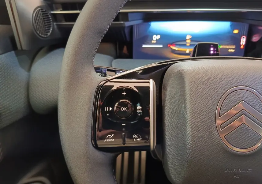 Gros plan sur le volant gris et noir du Citroën C5 Hybride 2026 avec commandes multifonctions et tableau de bord numérique lumineux.