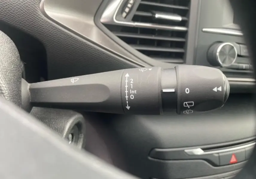 Gros plan sur la commande d'essuie-glace noire à gauche du volant dans l'habitacle d'une Peugeot 308 SW gris clair.