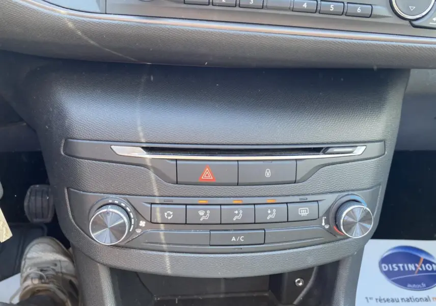 Tableau de bord central de Peugeot 308 SW gris clair, avec commandes de climatisation manuelle et boutons d'alerte visibles.