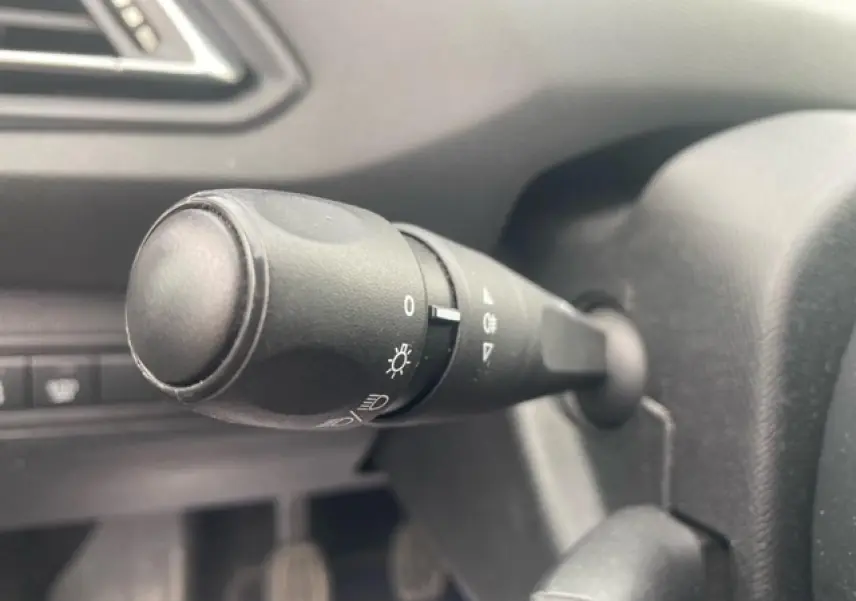 Gros plan sur la manette de commande des phares à gauche du volant dans l'habitacle d'une Peugeot 308 SW gris clair.