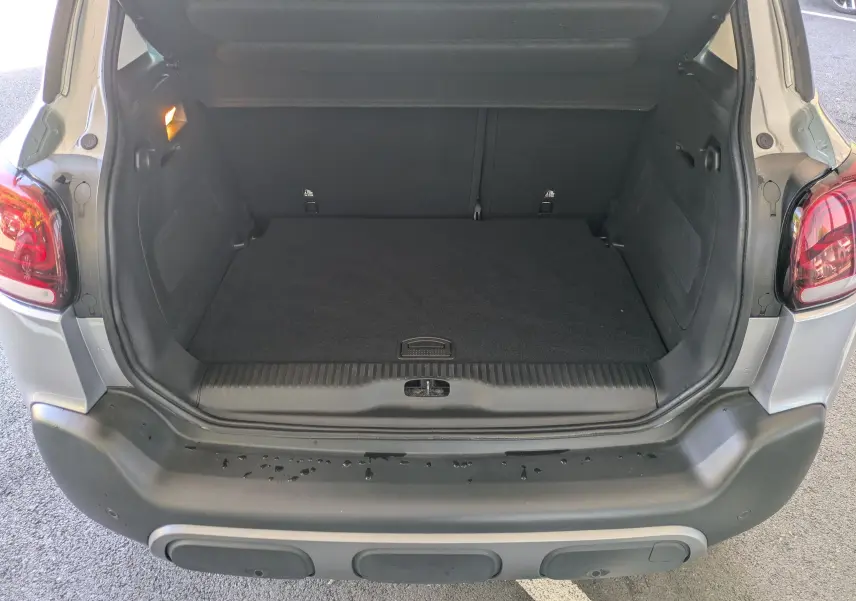 Coffre ouvert vu de l'arrière d'une Citroën C3 Aircross gris Artense, avec intérieur noir et feux arrière visibles.