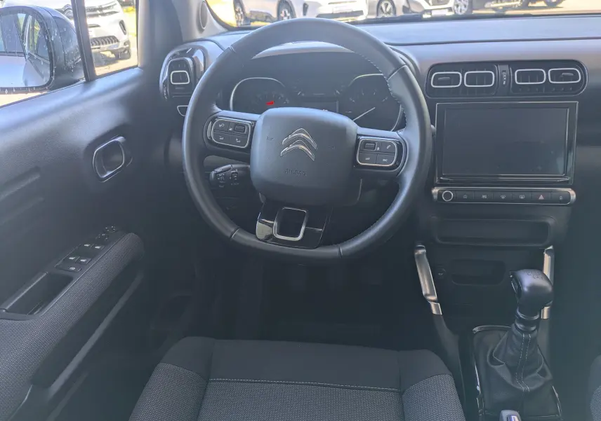 Intérieur avant droit du Citroën C3 Aircross gris, sièges tissu gris et volant cuir avec tableau de bord visible.