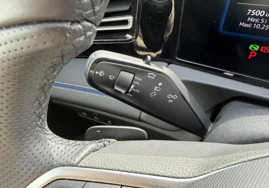 Gros plan sur la manette de commande des essuie-glaces et clignotants du Volkswagen Tiguan 2025, intérieur noir et surpiqûres bleues.