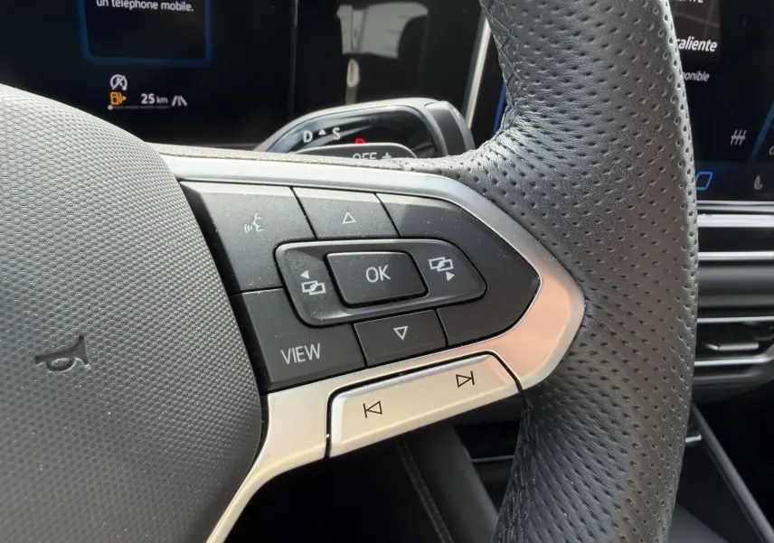 Gros plan sur le volant cuir perforé du Volkswagen Tiguan 2025 avec commandes multifonctions et écran digital en arrière-plan.
