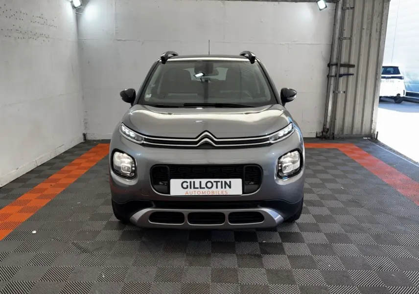 Vue frontale d'une Citroën C3 gris foncé avec calandre noire et feux LED, dans un garage éclairé.