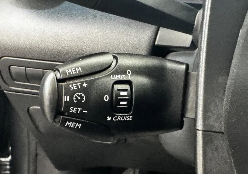 Gros plan sur la commande de régulateur de vitesse noire à gauche du volant dans une Citroën C3 gris foncé 2019.