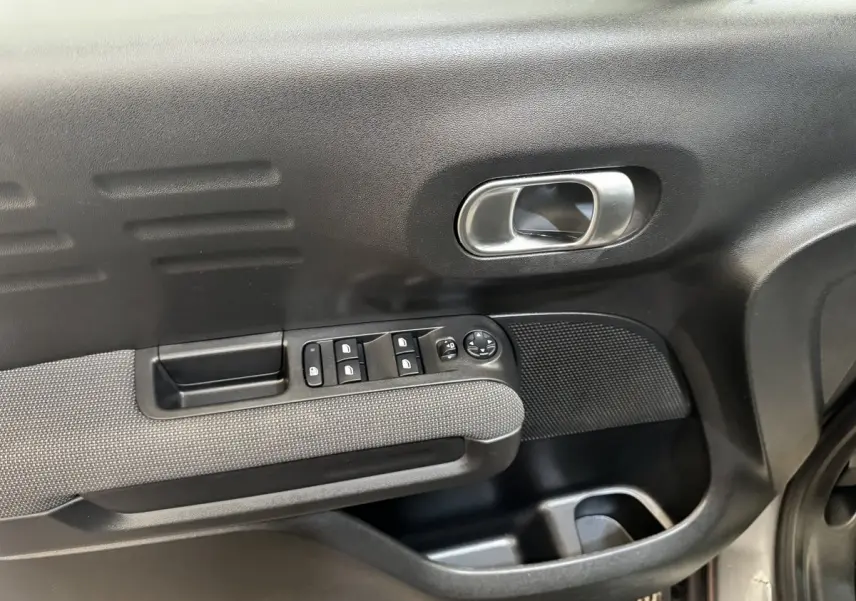 Gros plan sur la porte intérieure côté conducteur de la Citroën C3 gris foncé, avec commandes des vitres et poignée métallique.