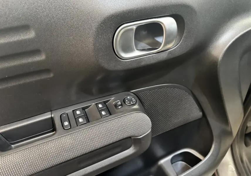 Gros plan sur la porte avant gauche de la Citroën C3 gris foncé, montrant les commandes de vitres et la poignée intérieure chromée.