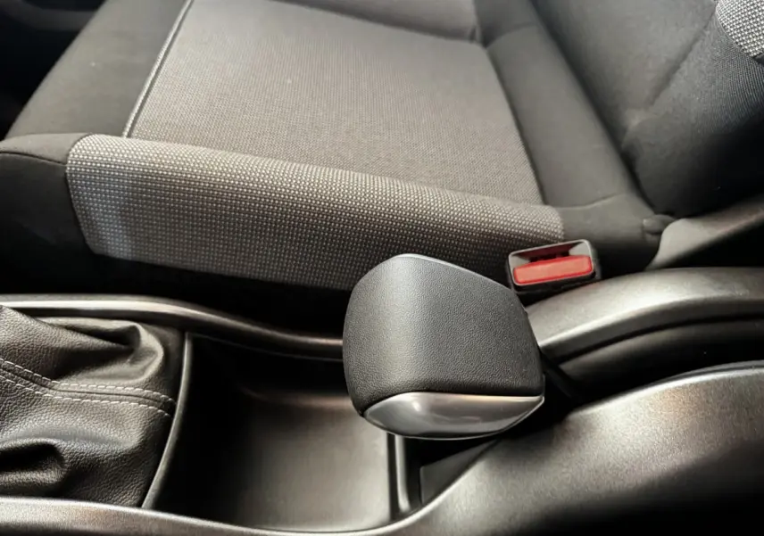 Gros plan sur le levier de frein à main noir et la console centrale, avec siège tissu gris foncé à côté dans une Citroën C3.