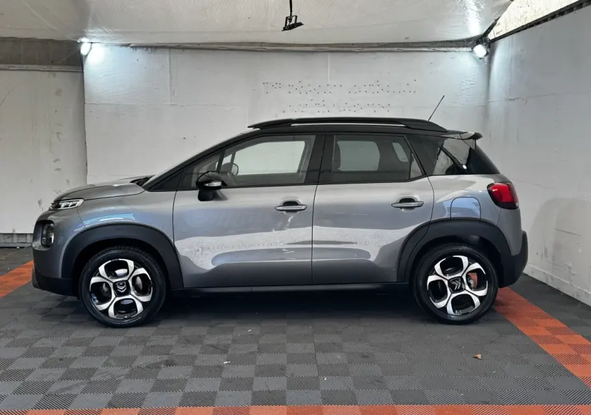 Profil droit d'une Citroën C3 gris foncé 2019 avec toit noir et jantes alliage distinctives en intérieur fermé.