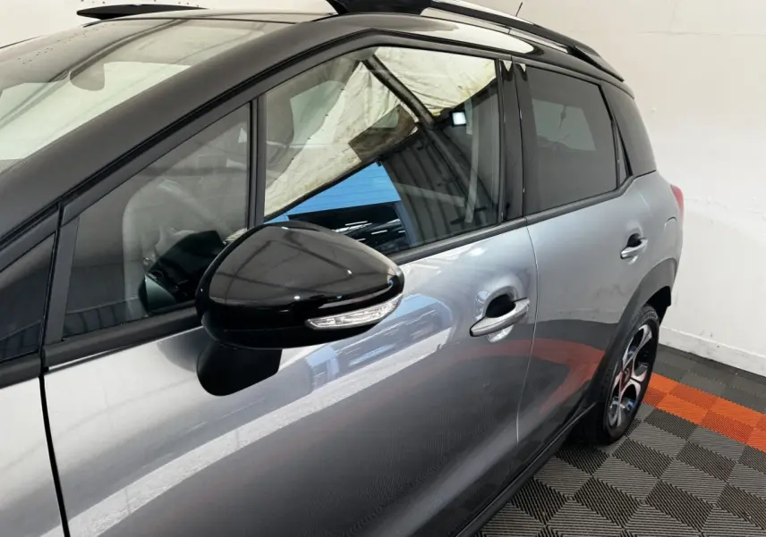 Vue latérale côté gauche d'une Citroën C3 gris foncé avec rétroviseur noir brillant et toit ouvrant partiel visible.