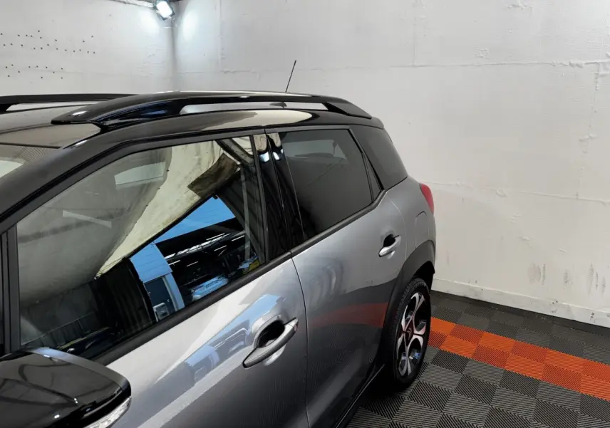 Vue latérale droite d'une Citroën C3 PureTech 110 gris foncé avec toit noir et jantes stylisées en intérieur.