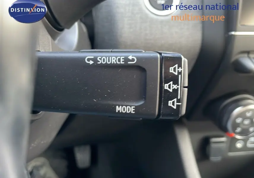Gros plan sur la commande au volant gauche de la Renault Clio noire étoile métal, avec boutons source et mode visibles.