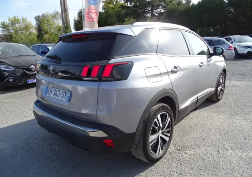 Vue 3/4 arrière droite d'un Peugeot 3008 gris Artense avec barres de toit en aluminium et feux arrière à griffes rouges.