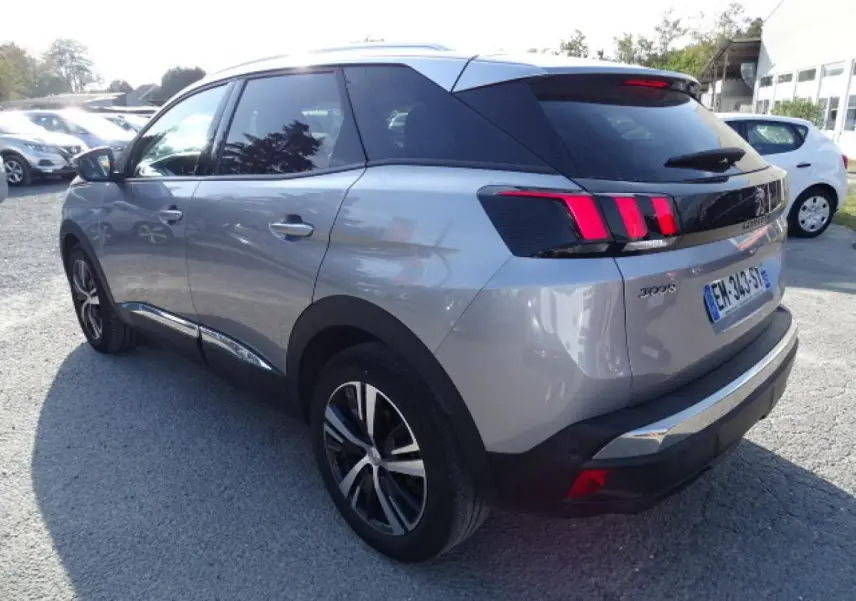 Vue 3/4 arrière gauche d'un Peugeot 3008 gris Artense avec barres de toit en aluminium et feux arrière à griffes rouges.