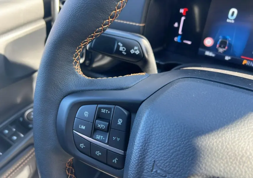 Gros plan sur le volant avec commandes multifonctions du Ford Ranger Wildtrak 2025, cuir noir et surpiqûres orange.