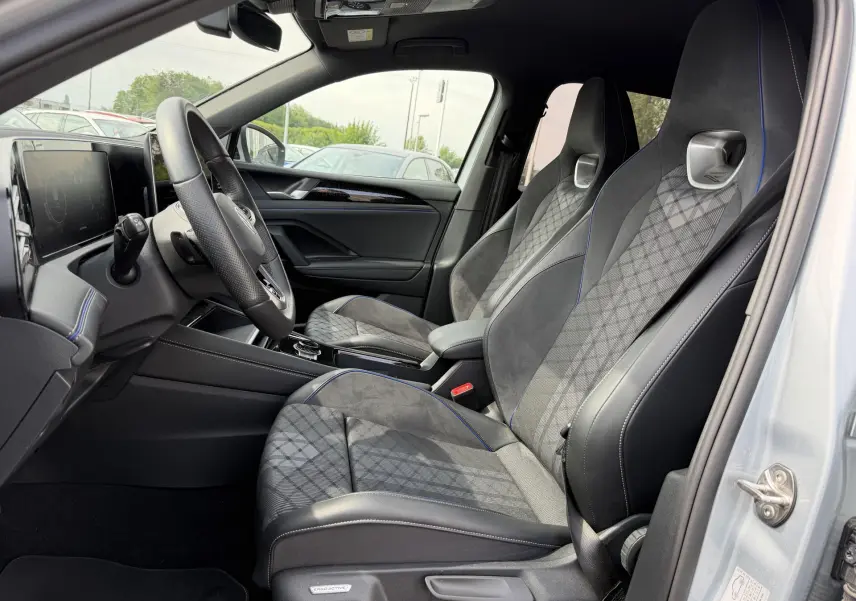 Vue intérieure côté conducteur du Volkswagen Tiguan gris 2025, sièges sport en tissu et alcantara avec surpiqûres bleues.