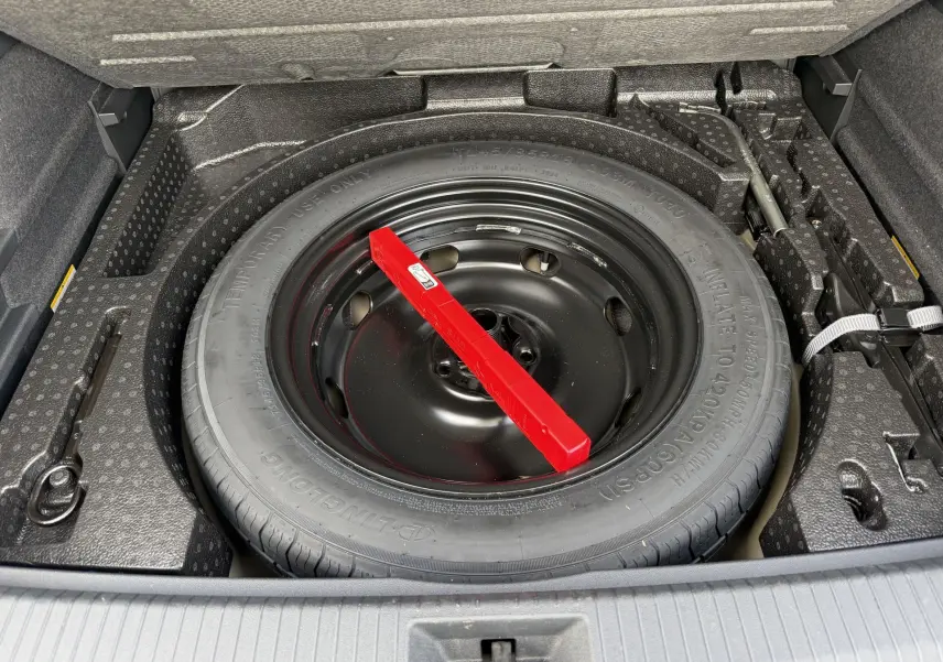 Gros plan sur la roue de secours compacte noire dans le coffre du Volkswagen Tiguan gris, entourée d’outils de bord.