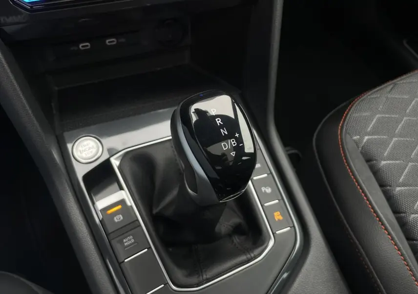 Le levier de vitesses automatique noir du SEAT Tarraco 2024, entouré de commandes et siège tissu gris à surpiqûres orange.