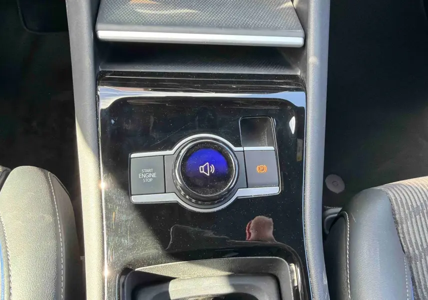 Vue plongeante sur la console centrale noire brillante du Volkswagen Tiguan 2025, avec bouton start/stop et frein à main électronique.