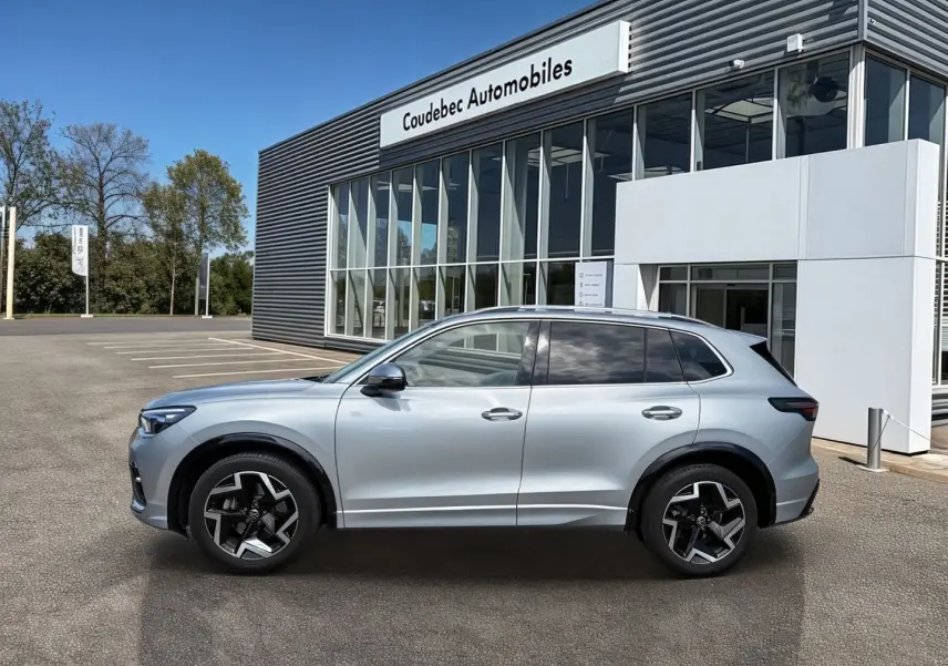 Vue de profil côté gauche d'un Volkswagen Tiguan gris métallisé avec jantes alliage noires devant un bâtiment de concession.