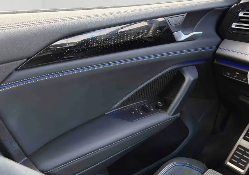 Vue intérieure côté gauche de la porte avant du Volkswagen Tiguan 2025 avec surpiqûres bleues et commandes électriques.