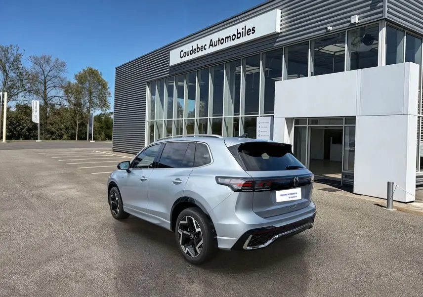 Vue 3/4 arrière du Volkswagen Tiguan gris métallisé 2025 avec jantes alliage noires devant un concessionnaire.