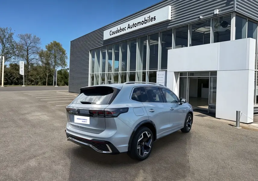 Volkswagen Tiguan gris en 3/4 arrière droit, avec jantes noires brillantes, stationné devant un concessionnaire.