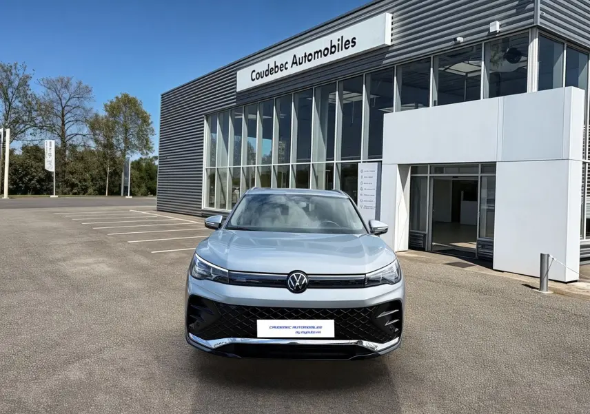 Vue avant d'un Volkswagen Tiguan gris 2025 garé devant un bâtiment moderne de concession automobile.
