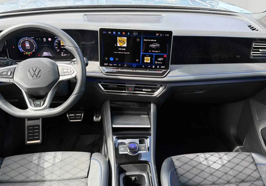 Vue intérieure avant du Volkswagen Tiguan 2025, tableau de bord noir avec écran tactile central et volant multifonction.