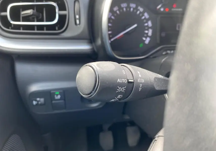 Gros plan sur la commande d'éclairage à gauche du volant dans l'habitacle d'une Citroën C3 gris clair de 2017.