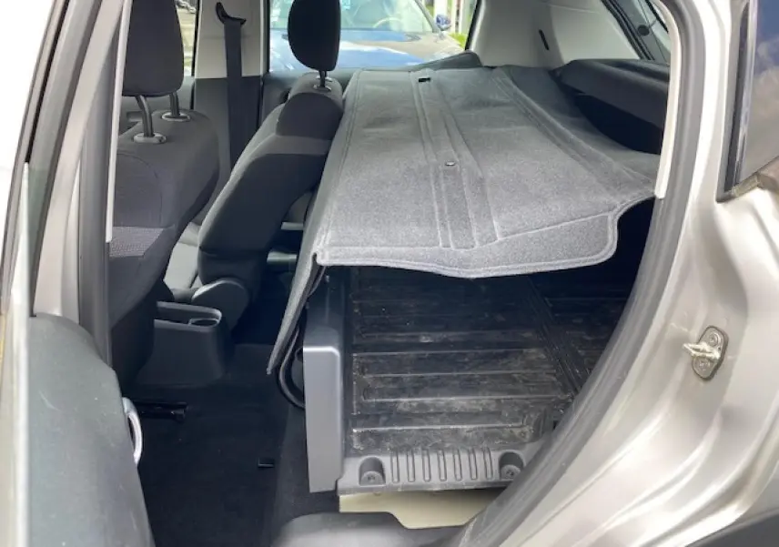 Vue intérieure côté droit d'une Citroën C3 gris clair 2017 avec siège arrière rabattue et tapis de coffre visible.