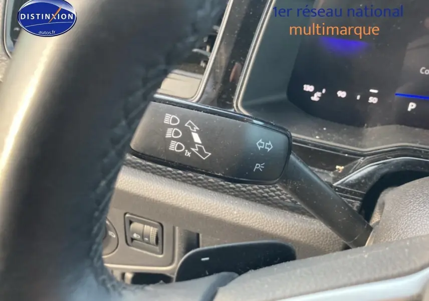 Gros plan sur le commodo gauche et le volant cuir de la Volkswagen Polo gris cendre, tableau de bord digital en arrière-plan.